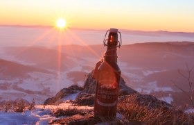 Eine Flasche Schneeberg Bräu Bier steht auf einem schneebedeckten Berg bei Sonnenuntergang.