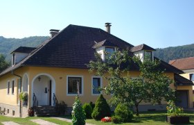 Ein gelbes Einfamilienhaus mit schwarzem Dach und Garten.