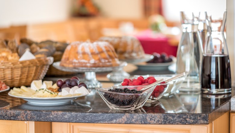 Frühstücksbuffet mit Kuchen, Beeren, Käseplatte und Getränken auf einem Tisch.