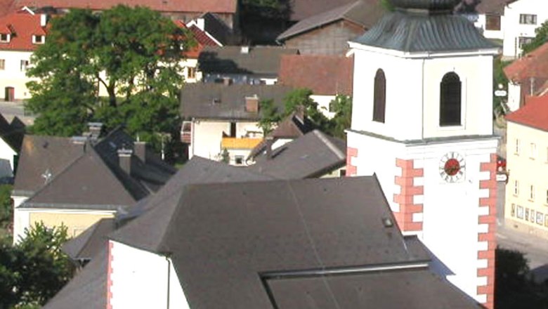 Pfarrkirche Hochneukirchen mit umliegenden Geb&auml;uden und Landschaft.