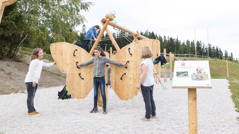 Kinder spielen auf einem großen Holzschmetterling auf einem Spielplatz im Freien.