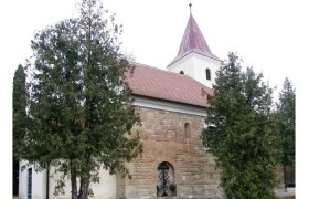 Historische Kirche mit rotem Dach und Turm, umgeben von Bäumen.