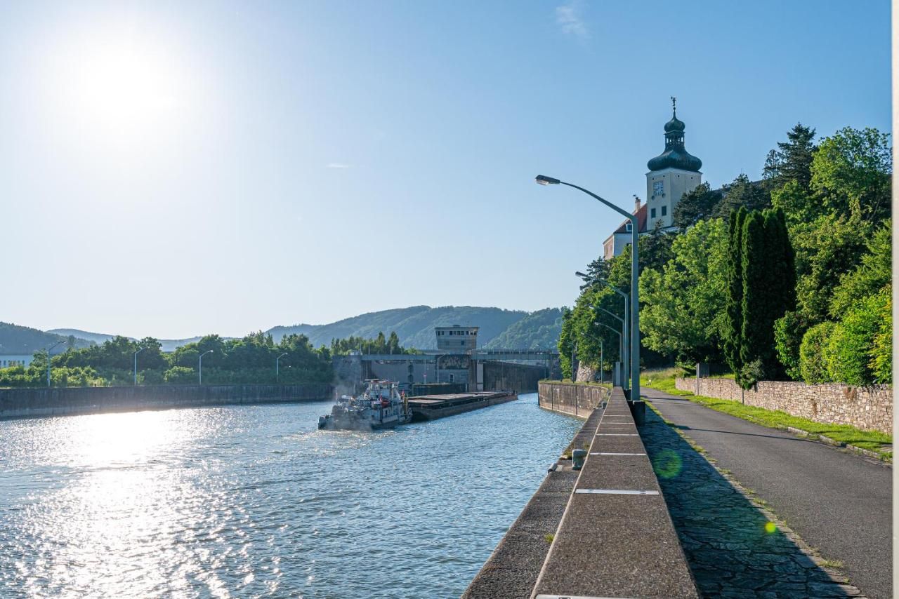 Fluss mit Schiff und Gebäude am Ufer, sonniger Himmel.