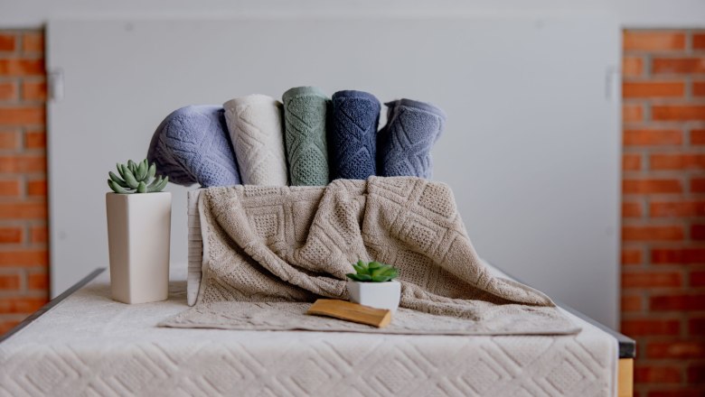 Farbige Handt&uuml;cher und Pflanzen auf einem Tisch vor einer Ziegelwand.