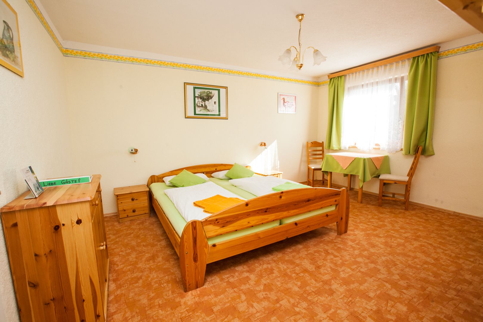 Gemütliches Gästezimmer mit Holzmöbeln, Doppelbett, Tisch und Stühlen, grüne Vorhänge und Dekoration.
