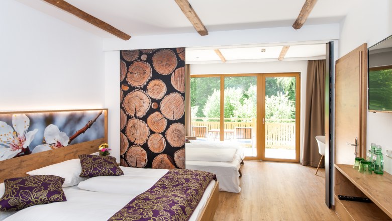 Ein modernes Familienzimmer mit Holzboden, zwei Betten, großen Fenstern und dekorativen Holzelementen.