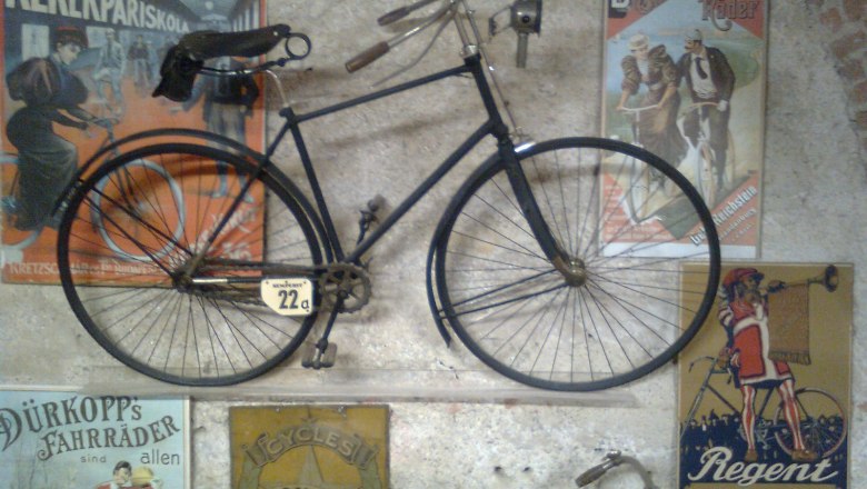 Altes Fahrrad an einer Wand mit Vintage-Werbeplakaten im Fahrradmuseum Schloss Vösendorf.