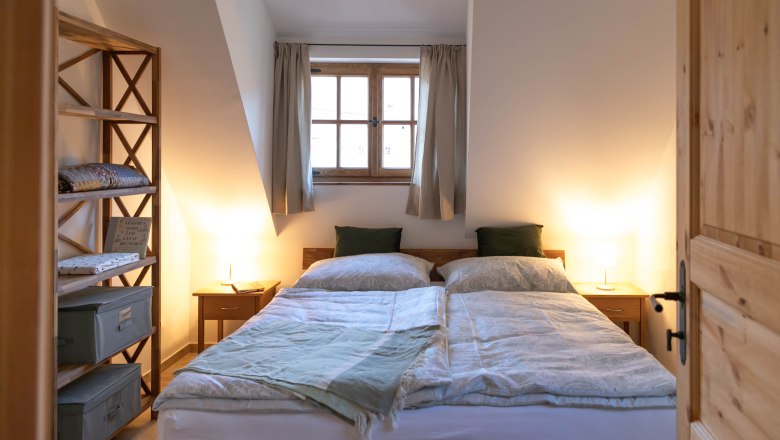 Gem&uuml;tliches Schlafzimmer mit Doppelbett, Holzm&ouml;beln und Fenster mit Vorh&auml;ngen.