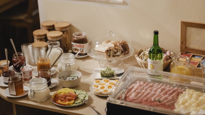 Frühstücksbuffet mit Brot, Aufschnitt, Obst und Getränken.
