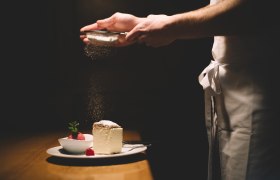 Ein Teller mit Cremeschnitte und Himbeersorbet, darüber wird Puderzucker gestreut.