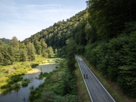 Sanfte H&uuml;gel umrahmen den idyllischen Radweg, der sich entlang des glitzernden Wassers schl&auml;ngelt. Die &uuml;ppige Vegetation und die ruhige Atmosph&auml;re laden dazu ein, die Natur in vollen Z&uuml;gen zu genie&szlig;en und die Seele baumeln zu lassen.