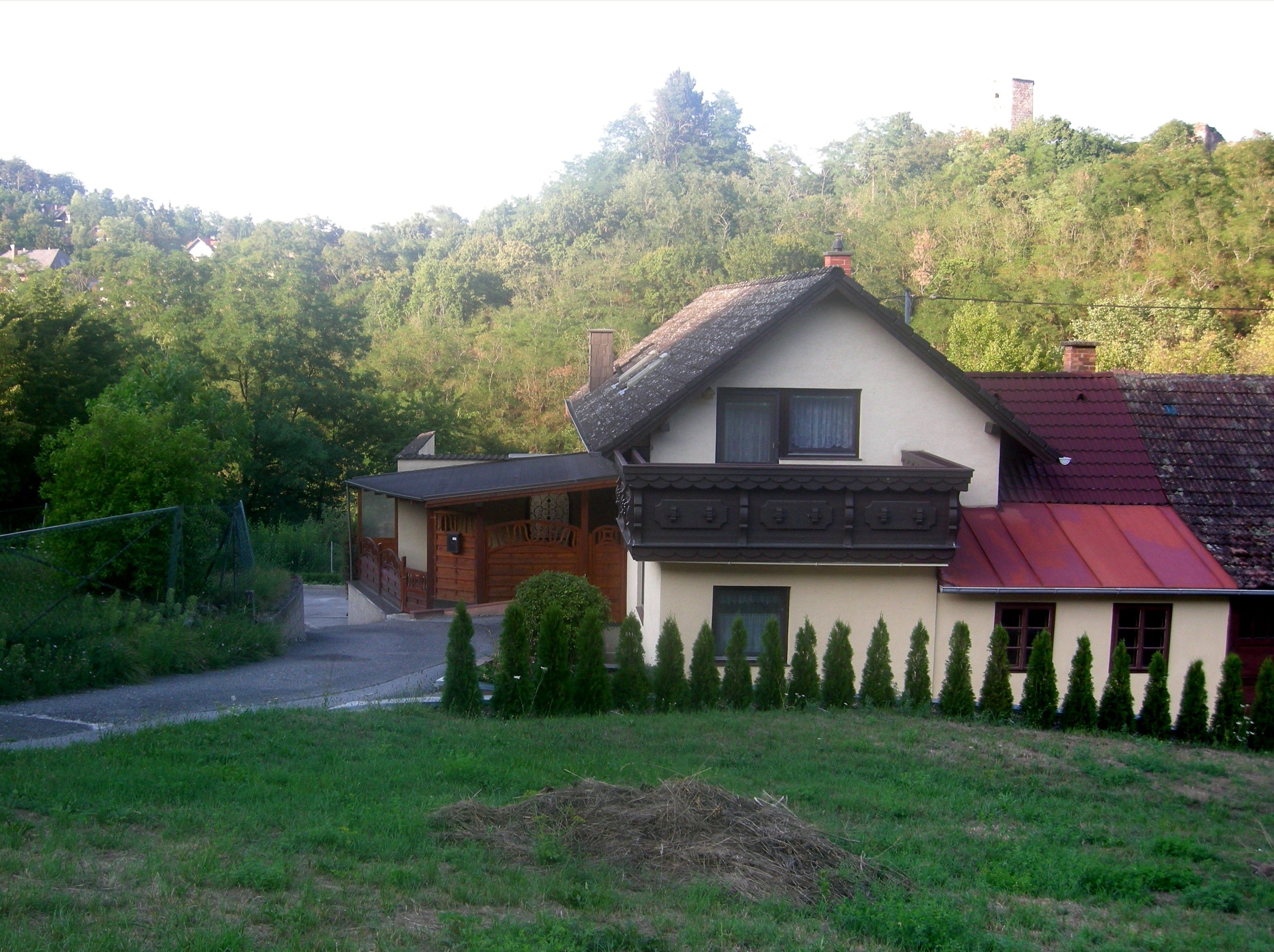 Ein Haus mit Balkon und Garten, umgeben von Bäumen und Hügeln.