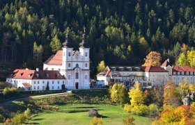 Die Wallfahrtskirche Maria Schutz vor einem bewaldeten H&uuml;gel im Herbst.