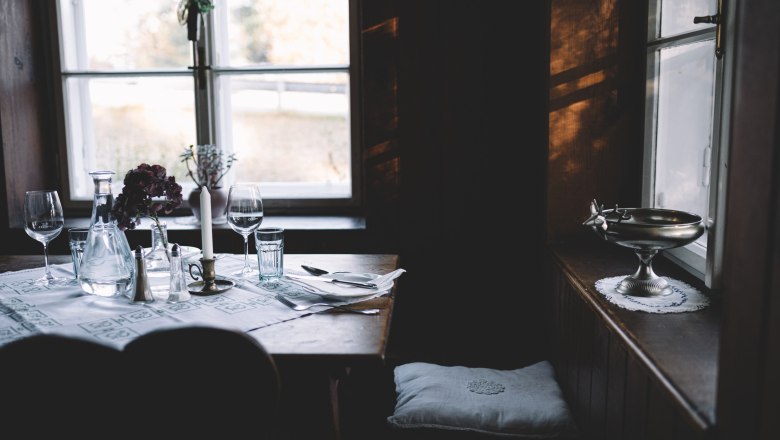 Gem&uuml;tlich gedeckter Tisch in einer rustikalen Stube mit Kerze und Weingl&auml;sern.