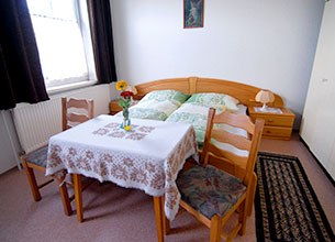 Gemütliches Zimmer mit Doppelbett, Tisch, zwei Stühlen und Blumen.
