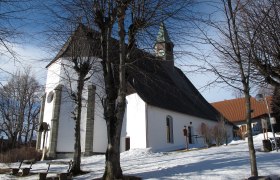 Pfarrkirche Maria Namen im Winter mit schneebedecktem Boden und kahlen Bäumen.