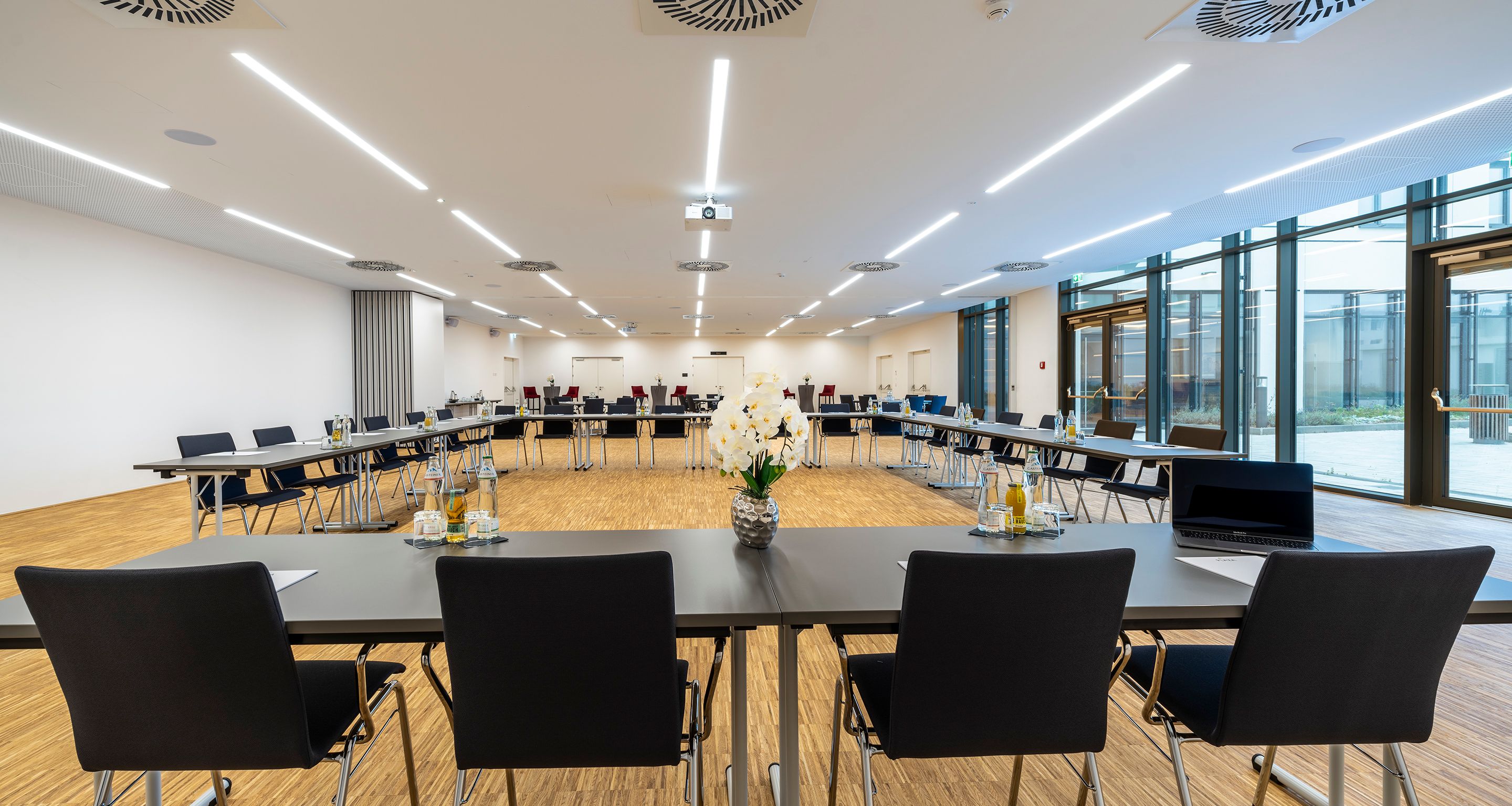 Großer, heller Raum mit schwarzer U-Bestuhlung 