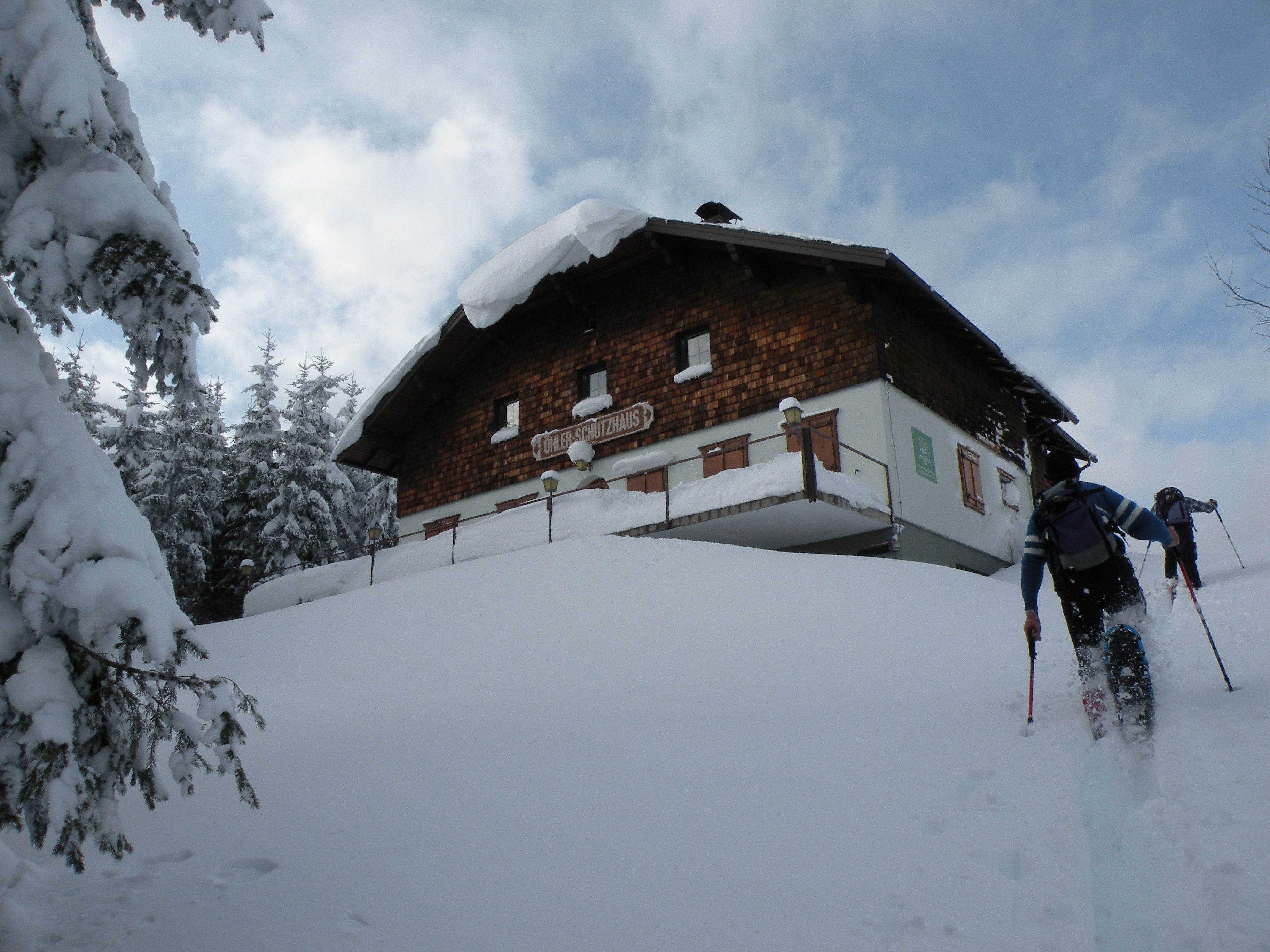 Zwei Personen steigen mit Skiern einen verschneiten Hang zum Öhlerschutzhaus hinauf.