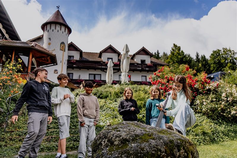Kinder spielen vor einem Hotel mit einem Schwert in einem Stein.