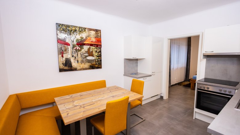 Moderne Küche mit gelber Eckbank, Holztisch und Kunstwerk an der Wand.