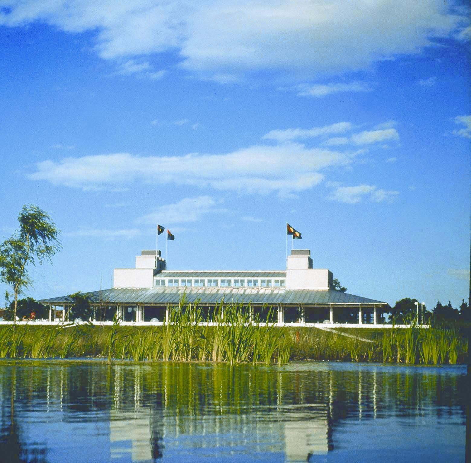 Gebäude des Golf Club Schloss Ebreichsdorf hinter einem Teich mit Schilf, blauer Himmel.