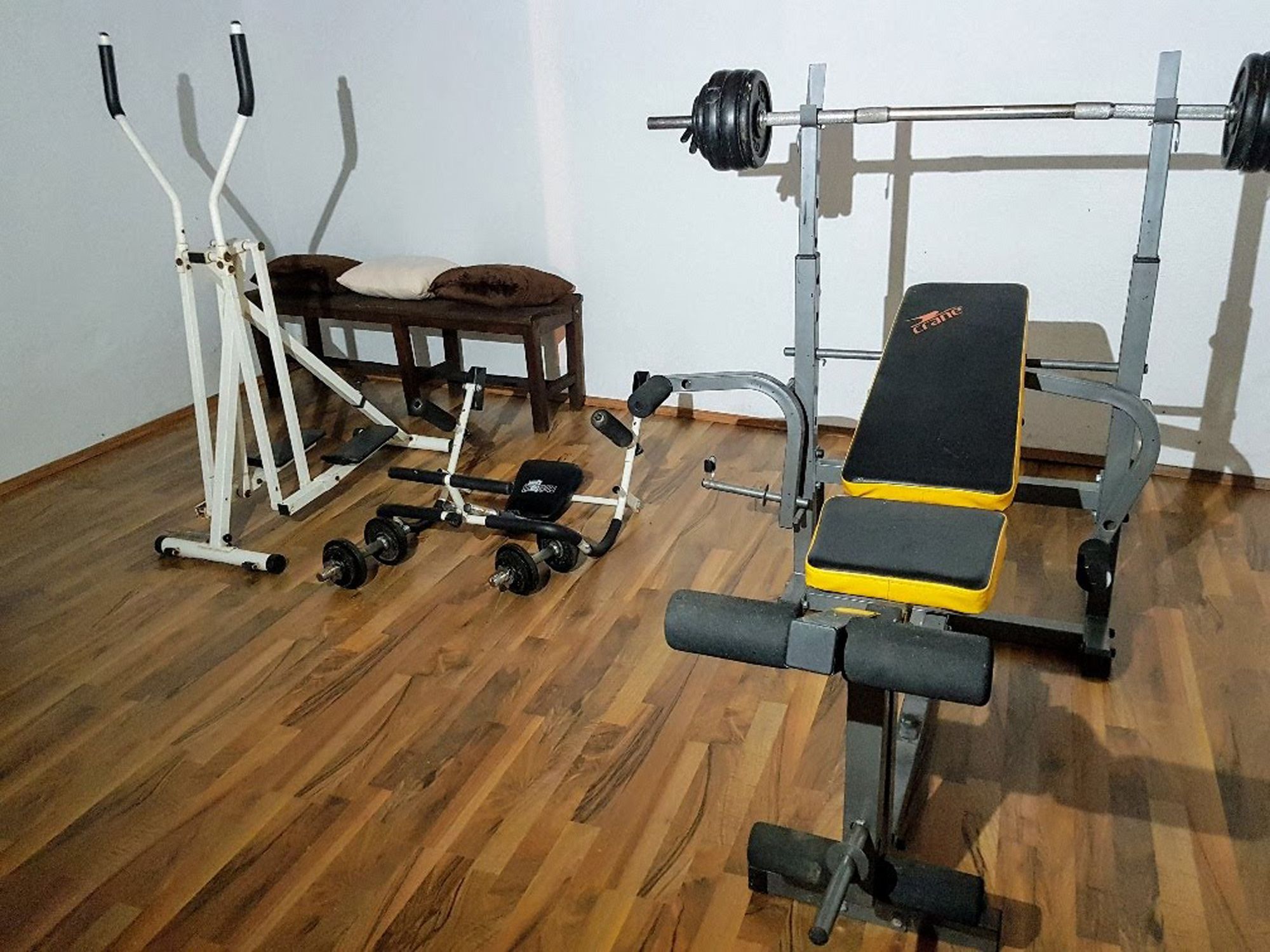Ein Fitnessraum mit Hantelbank, Crosstrainer und Hanteln auf Holzboden.