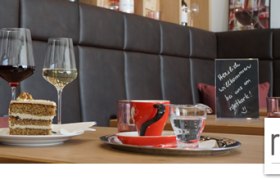 Innenansicht eines Caf&eacute;s mit Weingl&auml;sern, Kuchen und einer Tafel auf einem Tisch.