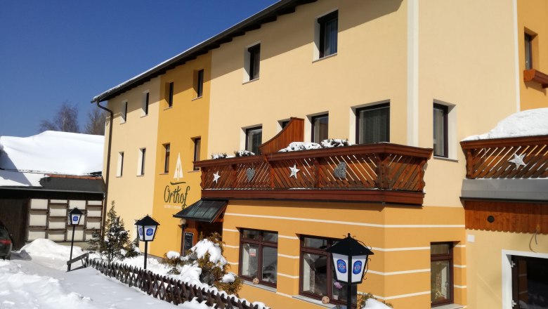 Gelbes Geb&auml;ude mit Holzbalkonen im Schnee, blauer Himmel.