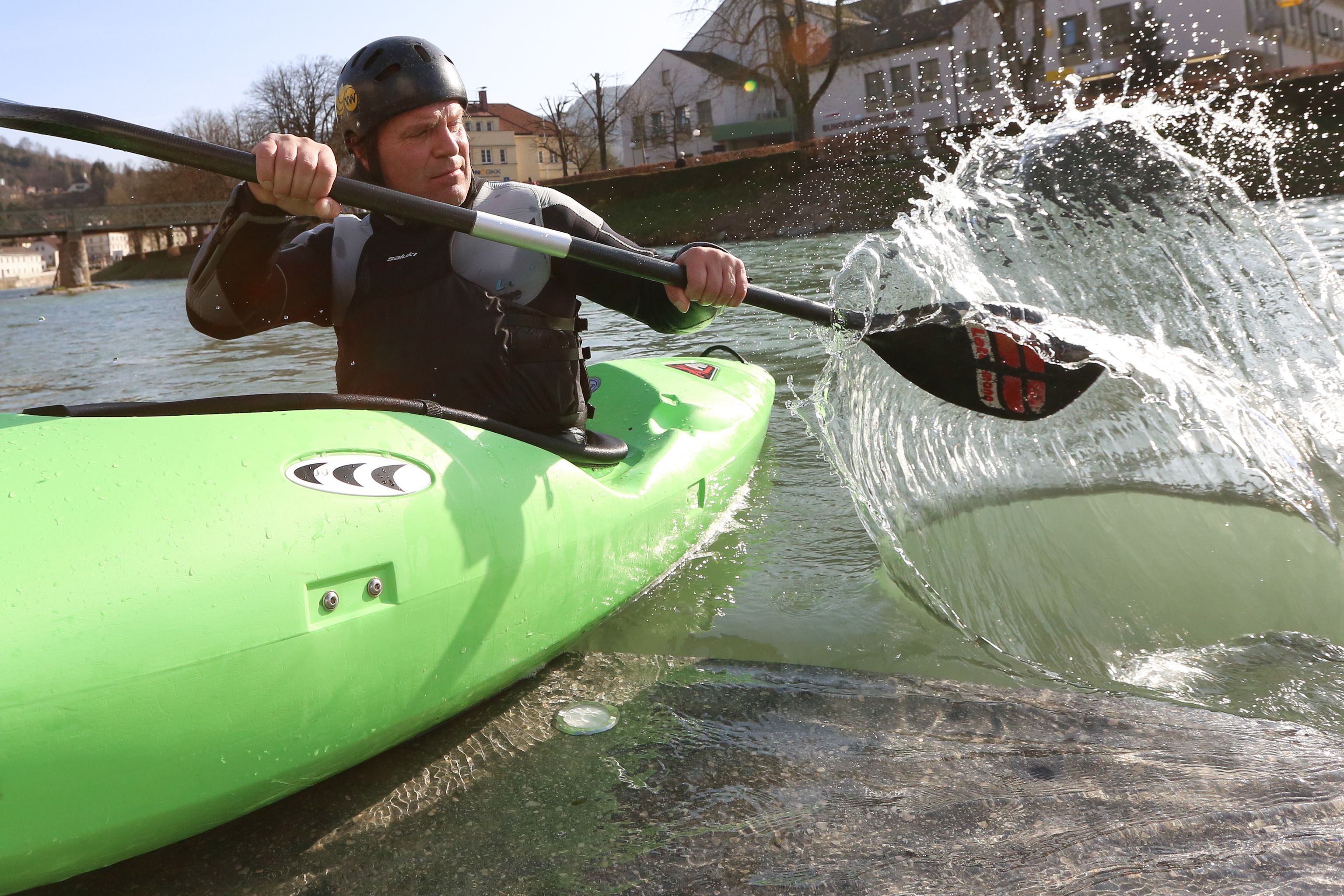 Person in grünem Kajak paddelt auf einem Fluss.