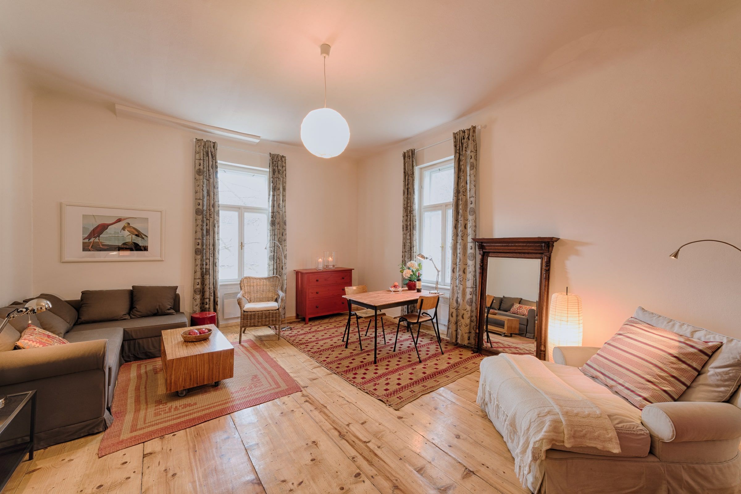 Gemütliches Wohnzimmer mit Holzboden, Sofa, Sessel, Esstisch und großem Spiegel.