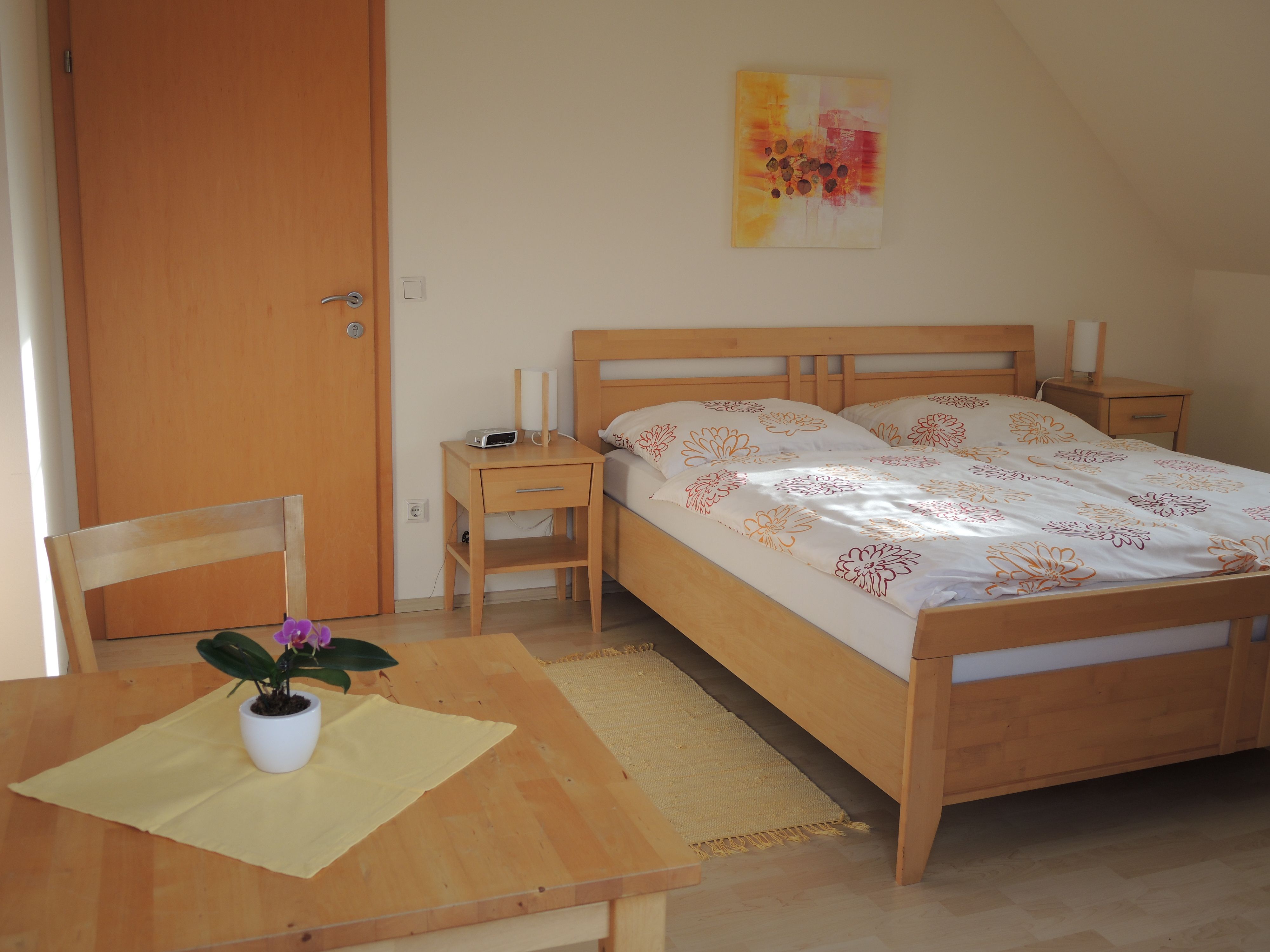 Ein Gästezimmer mit einem Doppelbett, zwei Nachttischen, einem Tisch mit Stuhl und einer Topfpflanze.