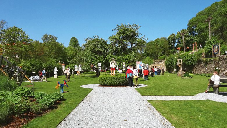 Besucher im Karikaturengarten Brunn am Wald, umgeben von Kunstwerken und grüner Landschaft.