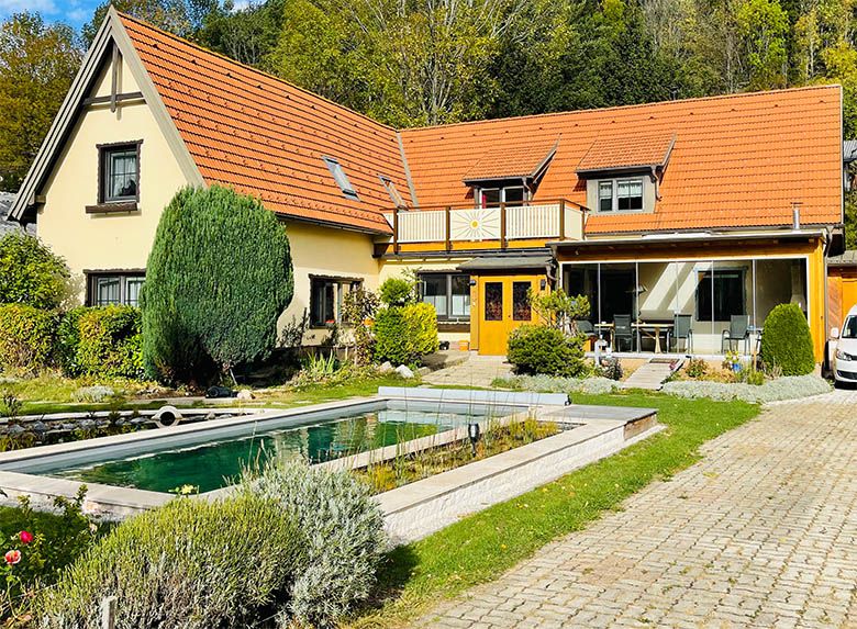 Ein gelbes Haus mit rotem Dach, Garten und kleinem Teich im Vordergrund.