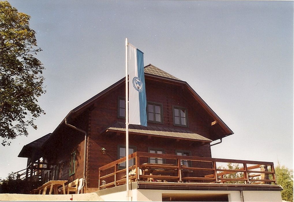 Holzhütte mit Fahne auf Terrasse, blauer Himmel.