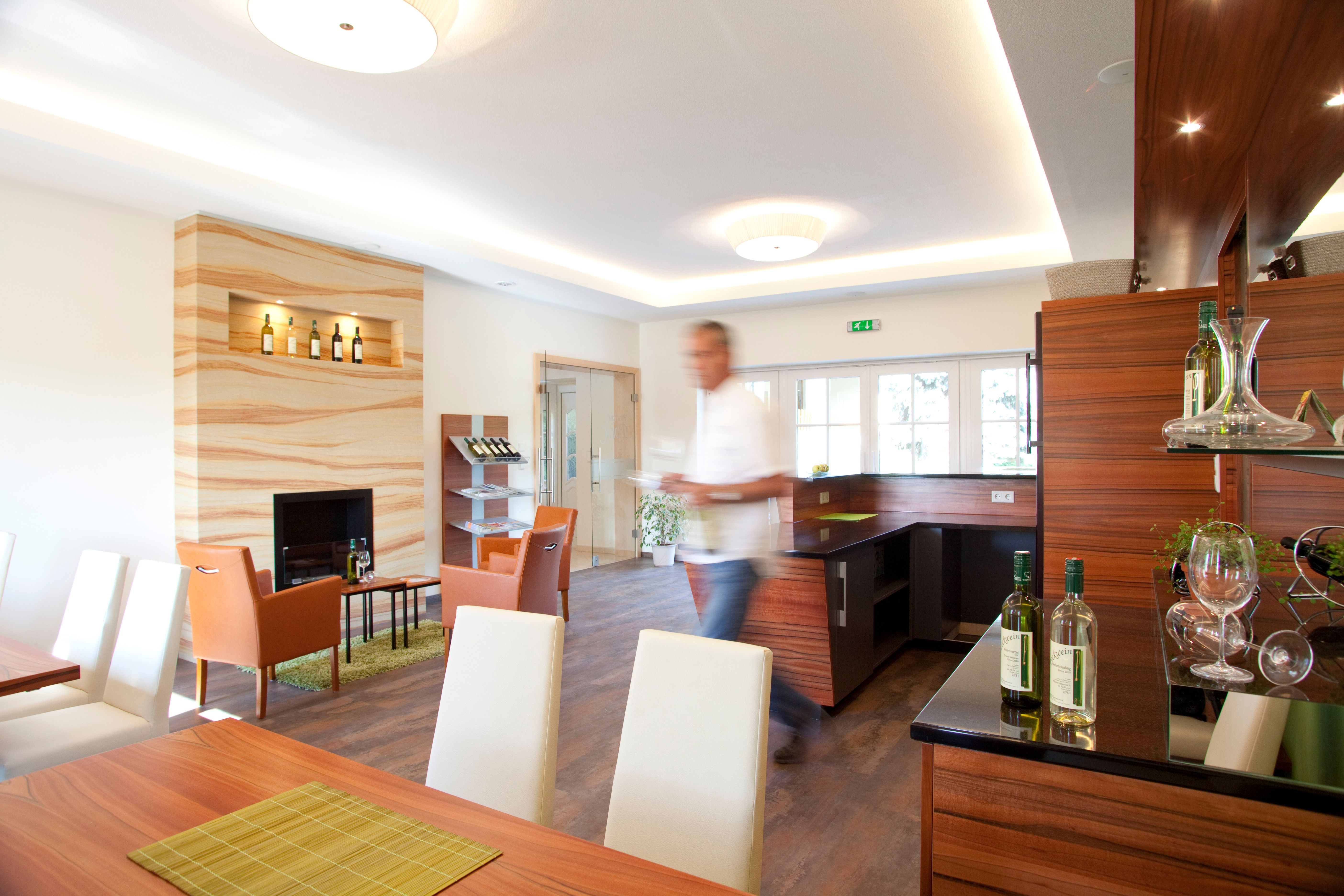 Ein moderner Verkostungsraum mit Holzmöbeln, Weinflaschen und einem unscharfen Mann im Vordergrund.