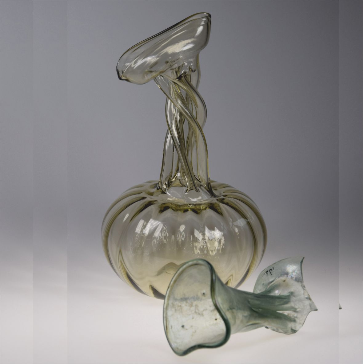 Glasobjekt mit verdrehten Formen auf grauem Hintergrund.