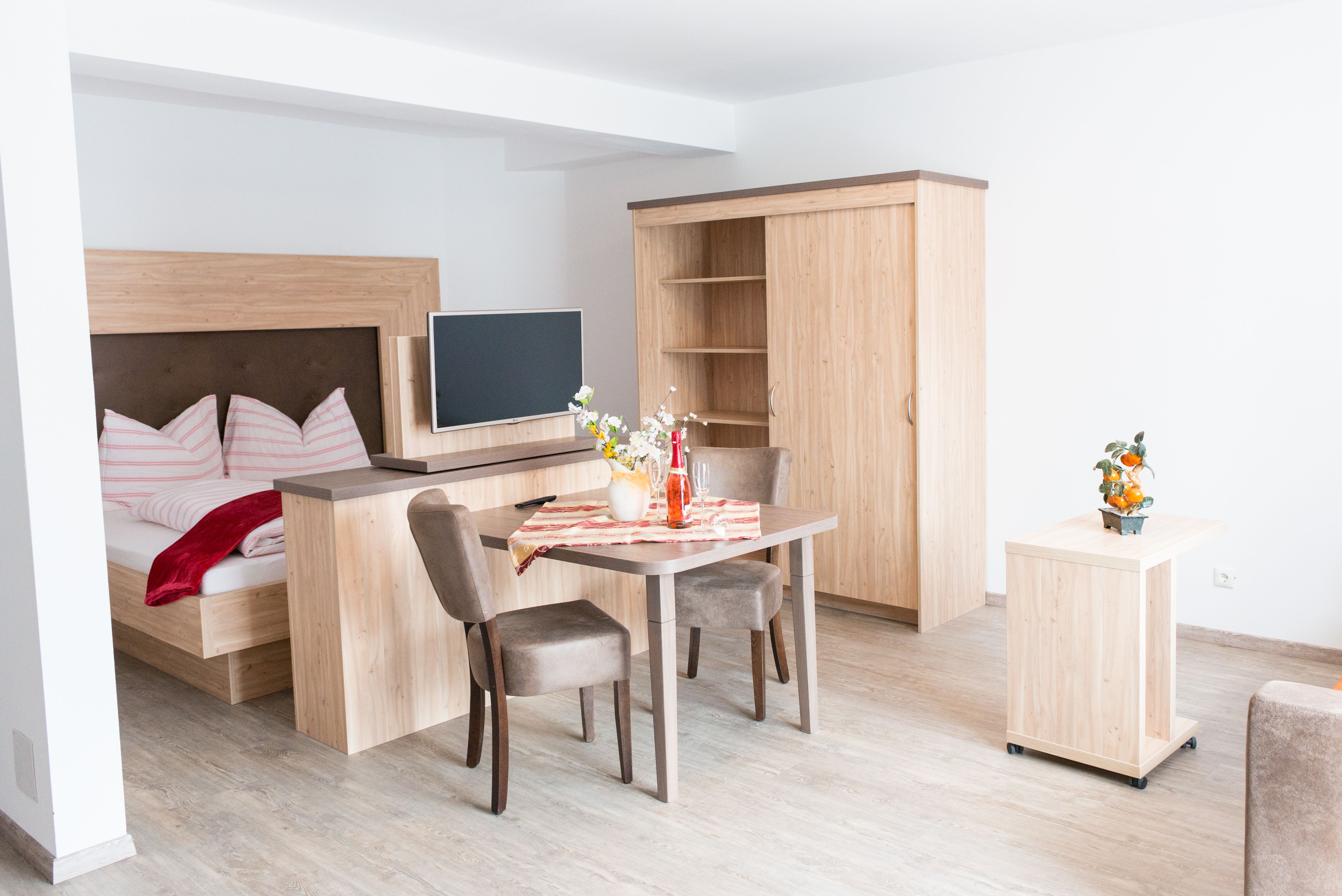 Modern eingerichtetes Apartment mit Holzmöbeln, Bett, Tisch und Fernseher.