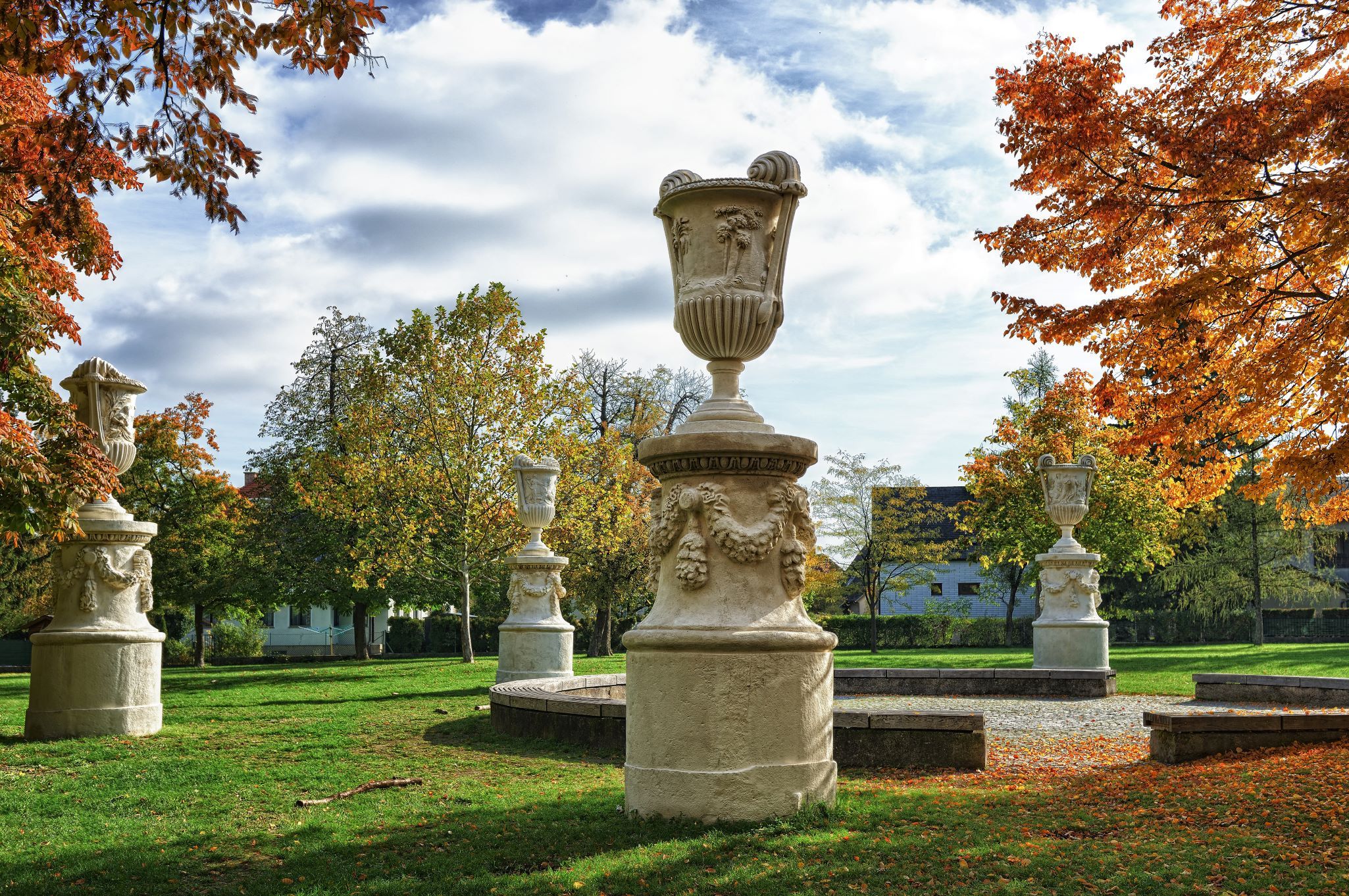 Steinskulpturen in einem herbstlichen Park mit buntem Laub und blauem Himmel.