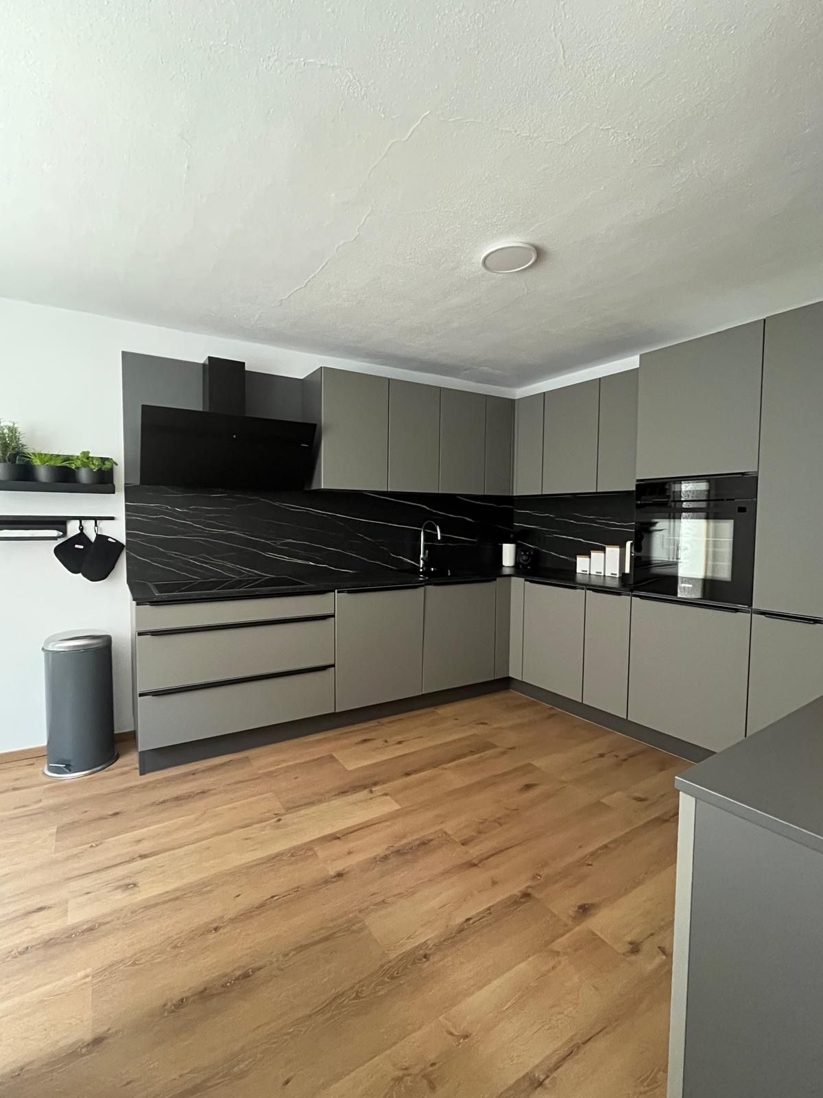 Moderne graue Küchenzeile mit schwarzen Arbeitsflächen und Holzfußboden.