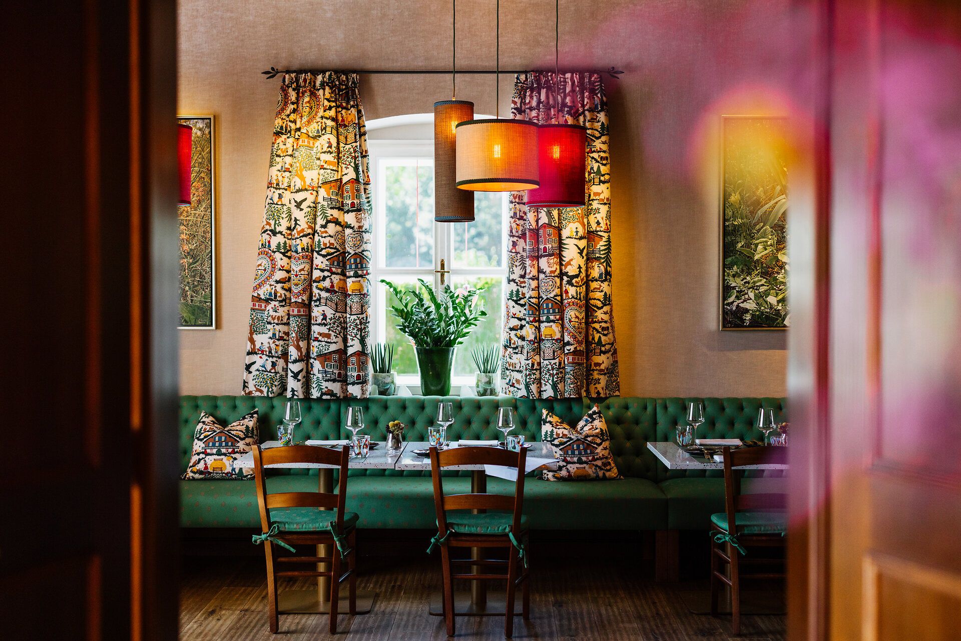 Gemütlicher Essbereich mit großen Fenstern, grünen Polstermöbeln und Pflanzen, mit Blick auf die Landschaft.