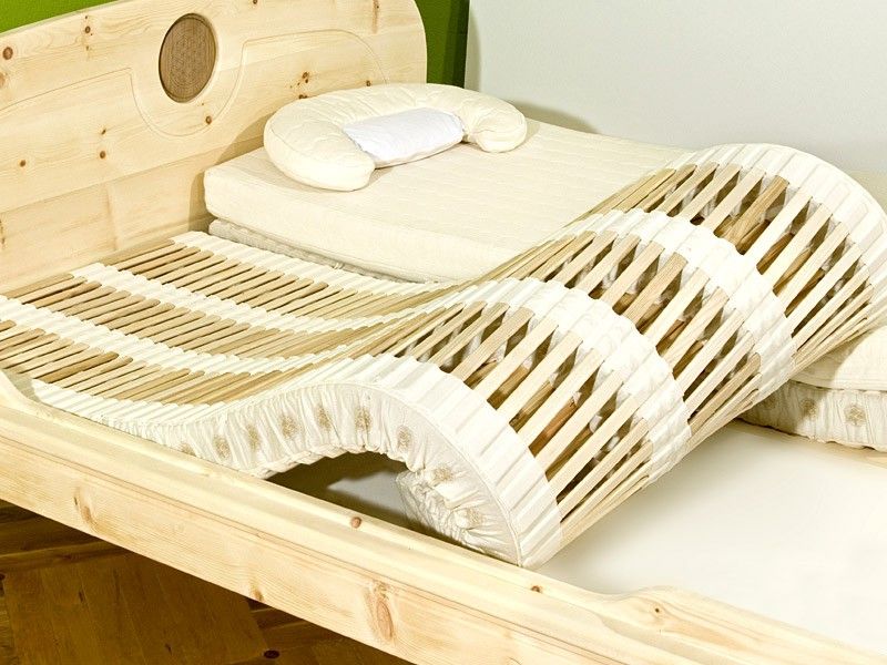 Ein Bett mit wellenförmigem Lattenrost und hellem Holzrahmen.