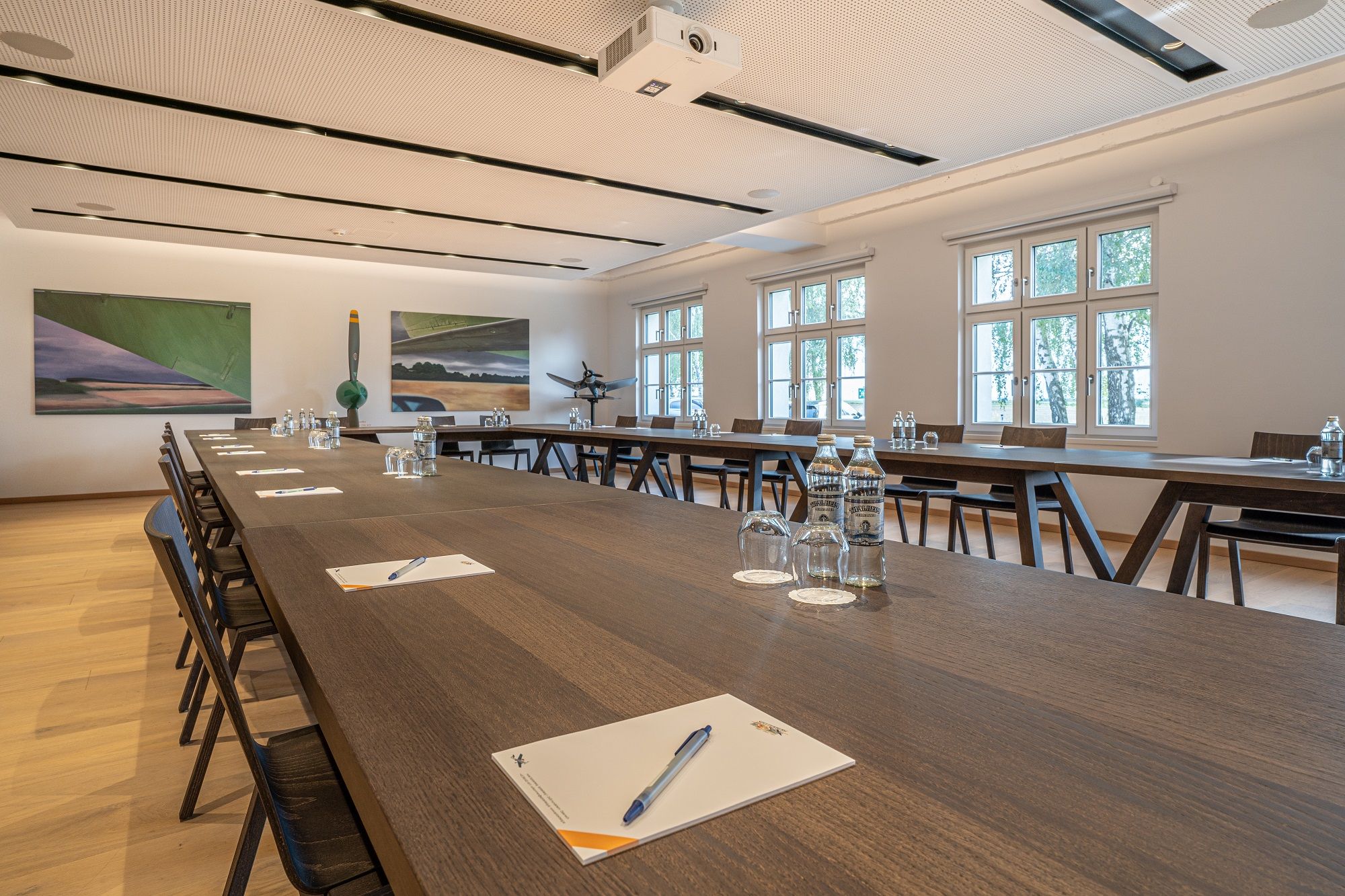 Seminarraum im Hotel Spitzerberg mit langen Holztischen, Stühlen, Wasserflaschen und Schreibmaterialien.