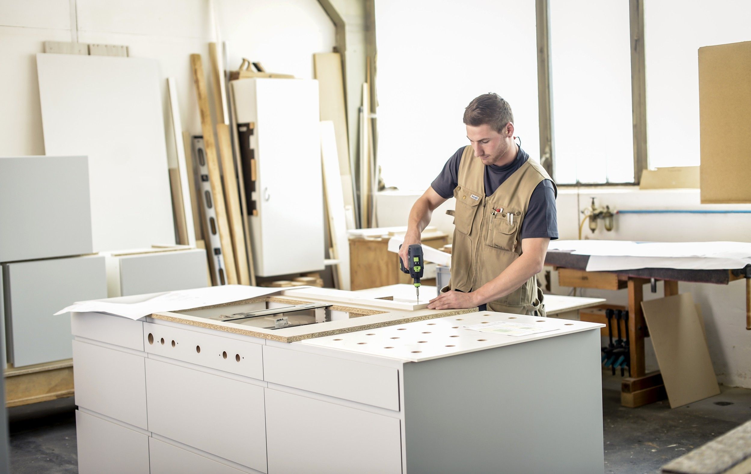 Ein Handwerker arbeitet in einer Werkstatt an einem Möbelstück mit einem Akkuschrauber.