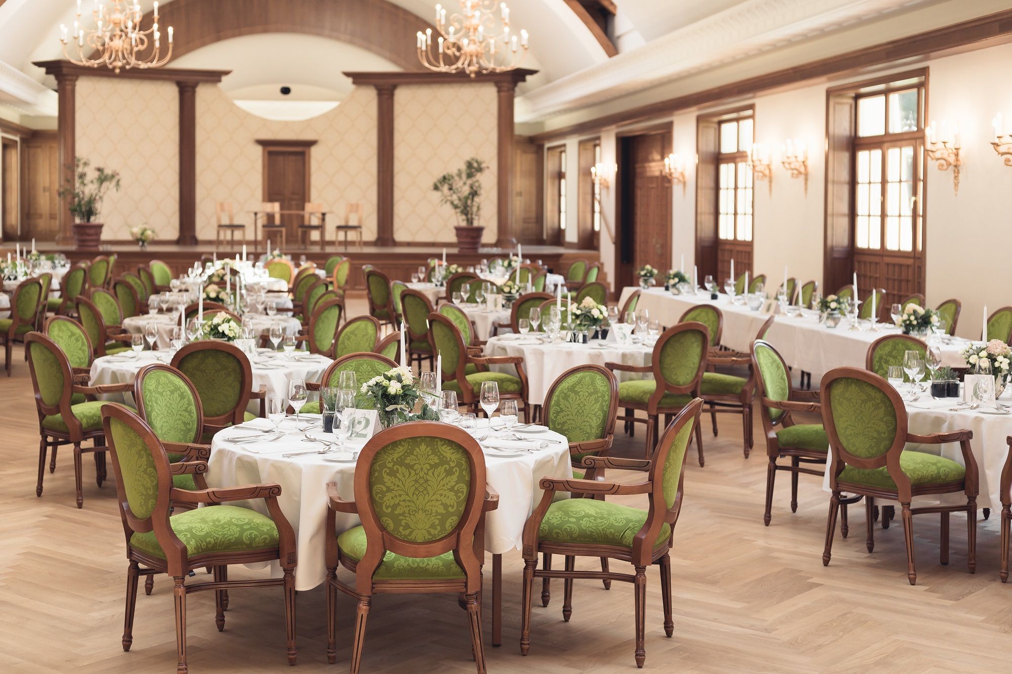 Eleganter Festsaal mit gedeckten Tischen und grünen Stühlen im Schloss Thalheim.