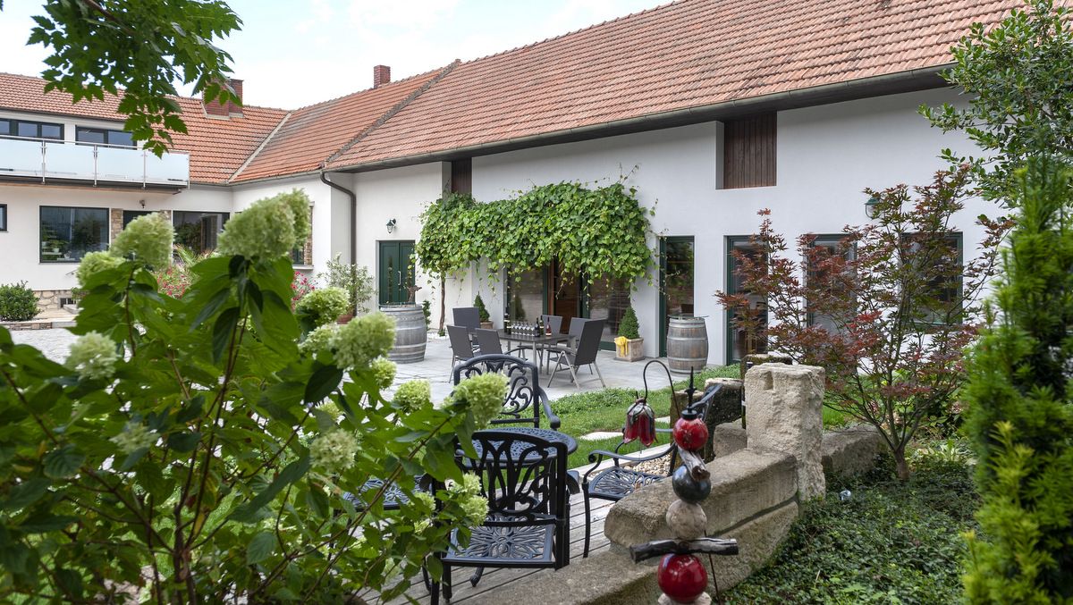Ein gemütlicher Innenhof eines Winzerhofs mit Pflanzen, Gartenmöbeln und Weinfässern.