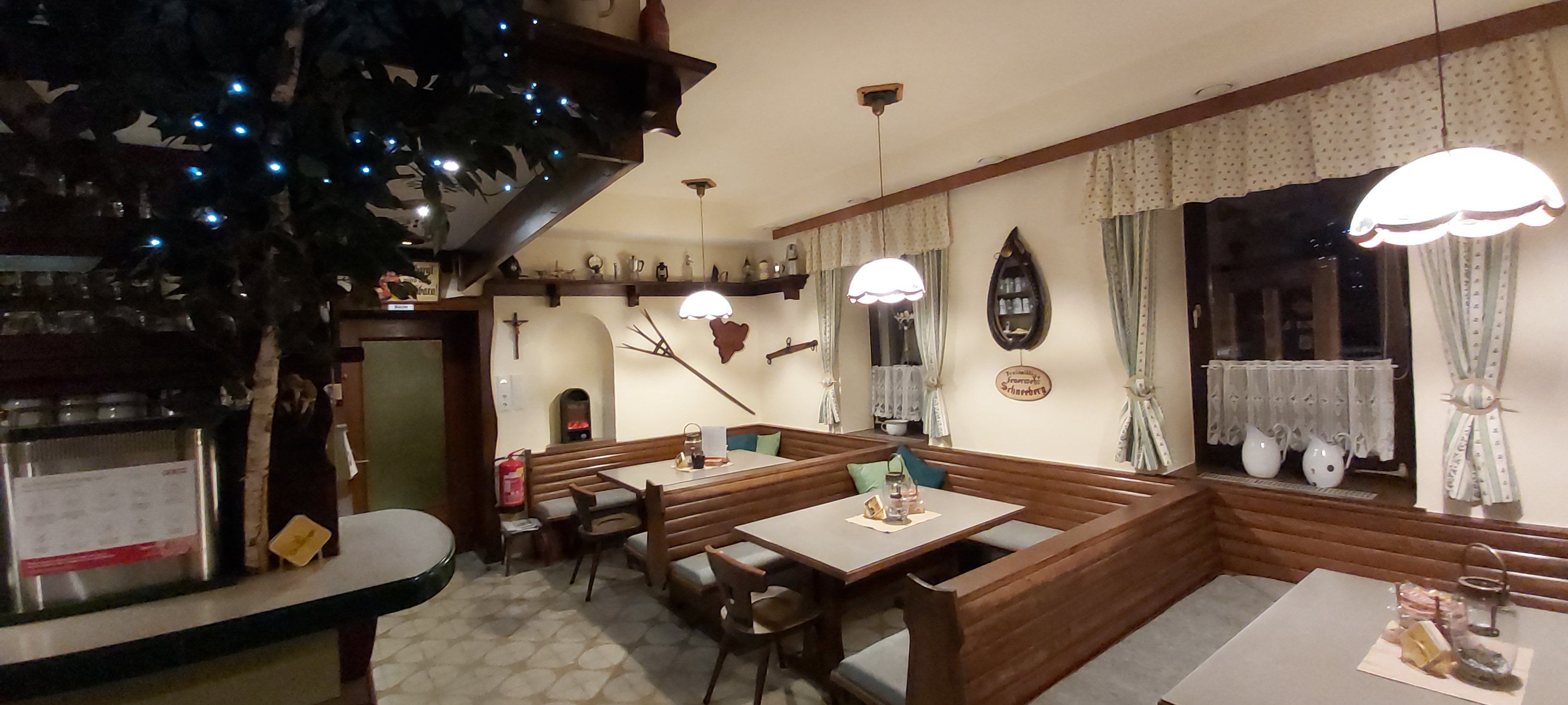 Gemütliche Gaststube mit Holzmöbeln, dekorativen Vorhängen und rustikalen Accessoires.