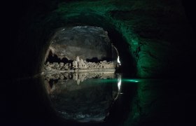 Dunkle Höhle mit Wasser und Felsformationen, beleuchtet von grünlichem Licht.