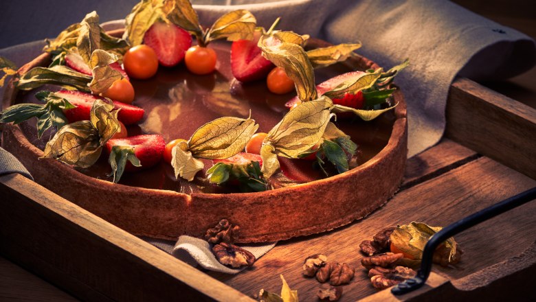 Eine Torte mit Schokoladenglasur, dekoriert mit Erdbeeren und Physalis, auf einem Holztablett.