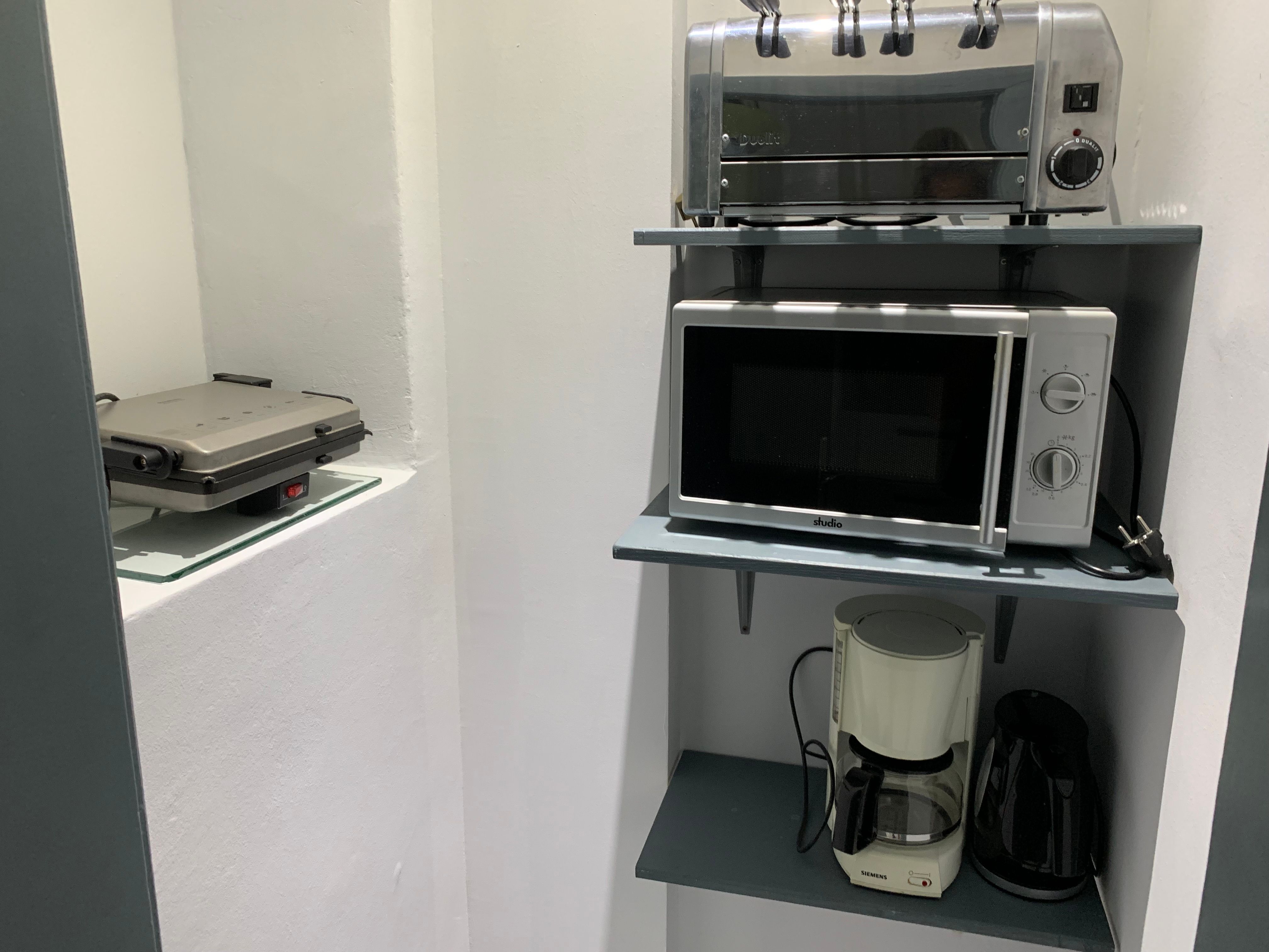 Küchenregal mit Toaster, Mikrowelle, Kaffeemaschine und Wasserkocher.