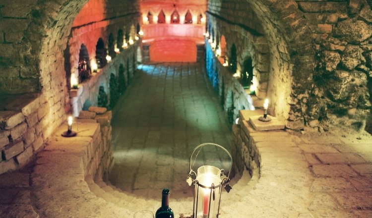 Ein stimmungsvoll beleuchteter Weinkeller mit Kerzen, einer Weinflasche und einem Glas auf einem steinernen Vorsprung.